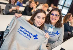 Two smiling students hold up university branded clothing